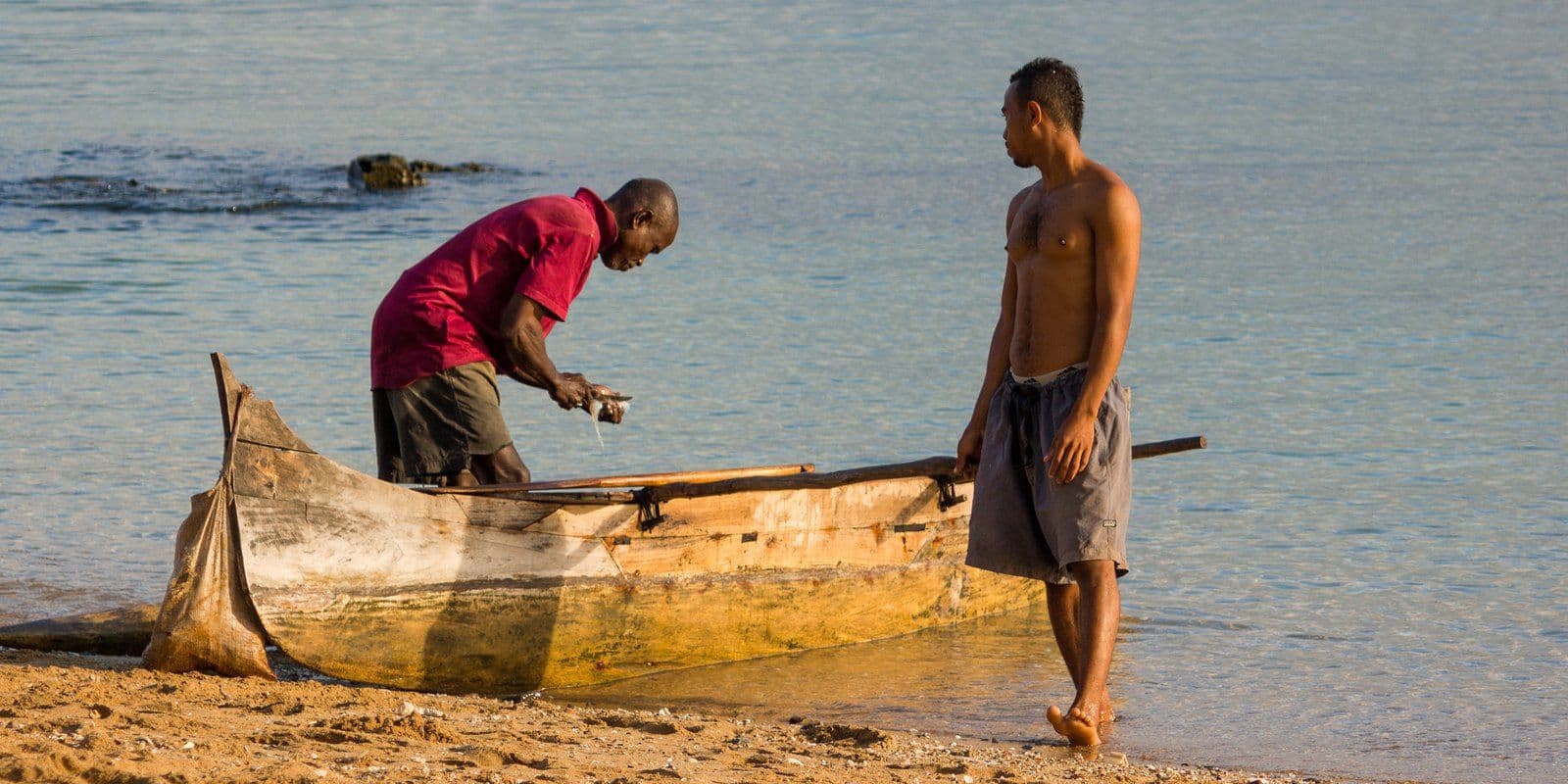 Deux pêcheurs devant leur pirogue sur une plage de Madagascar